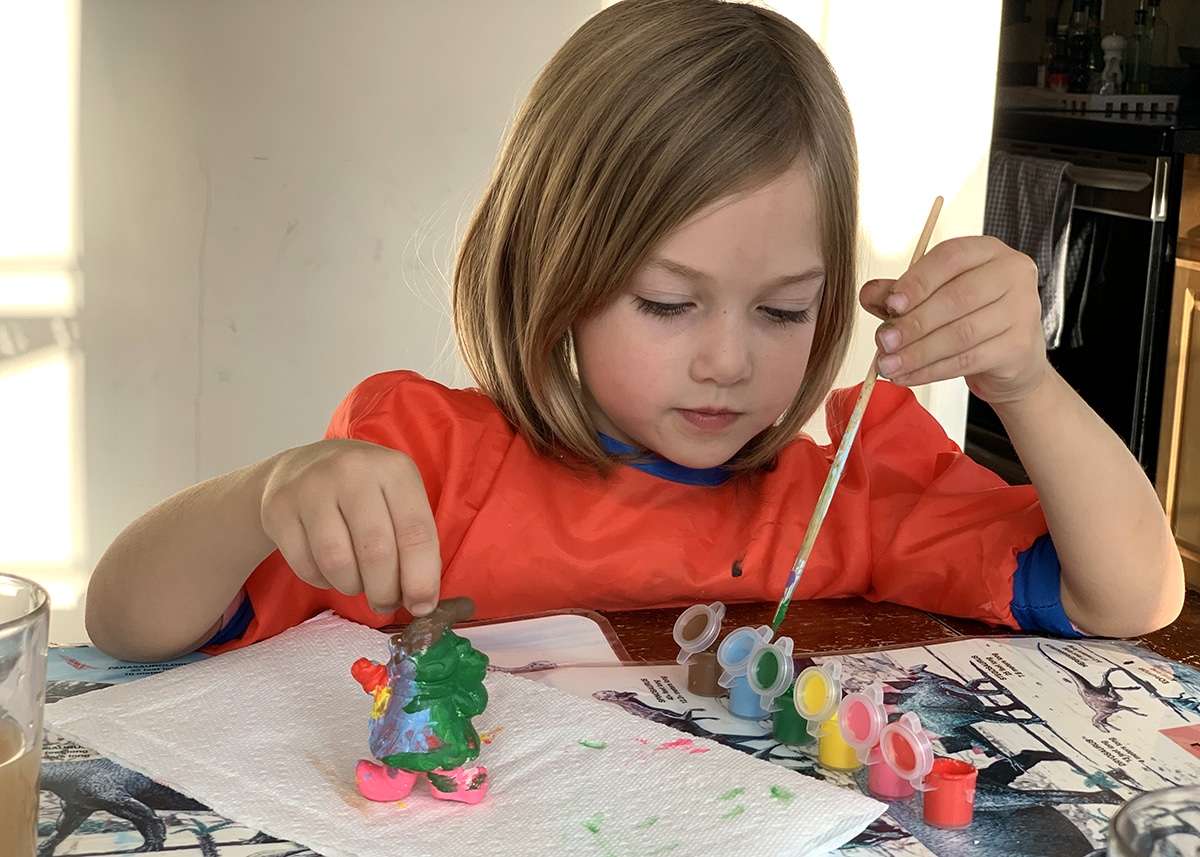 Child painting a ceramic figurine as part of a DIY advent calendar craft.